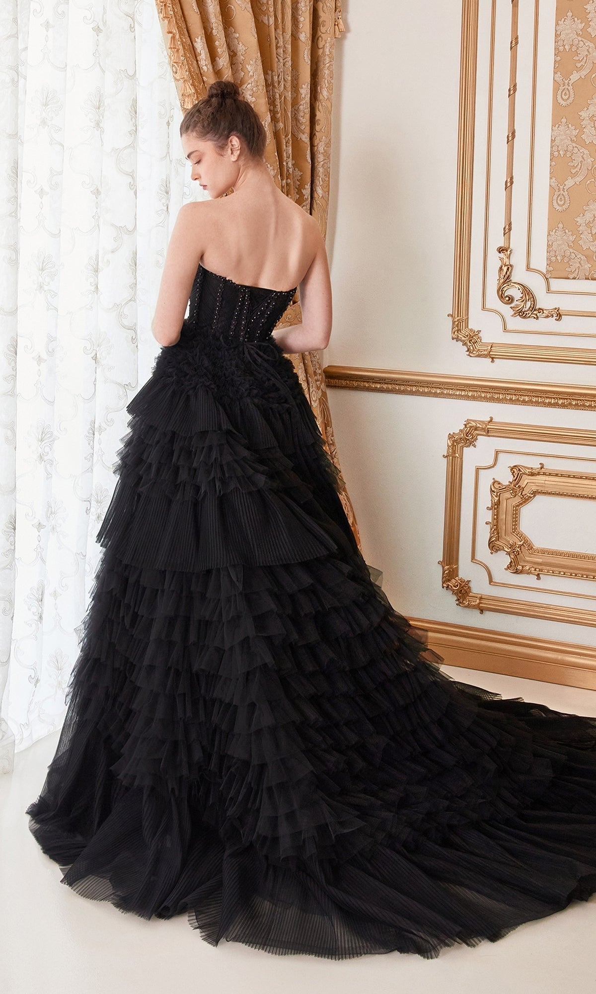 A woman in the Strapless Tiered Long Prom Ball Gown A1017 stands with her back to the camera in an ornate room featuring gold accents and patterned curtains.